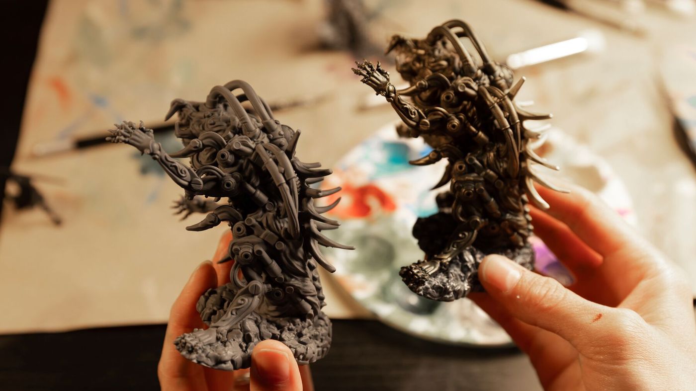 Two unpainted printed miniatures held in a hand