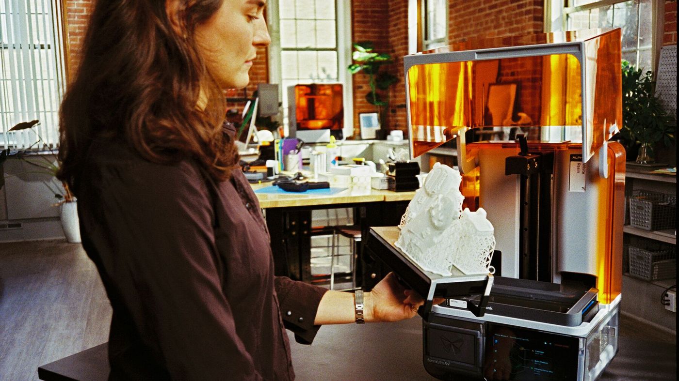 A person lifting a finished print on the build platform out of Form Studio 1