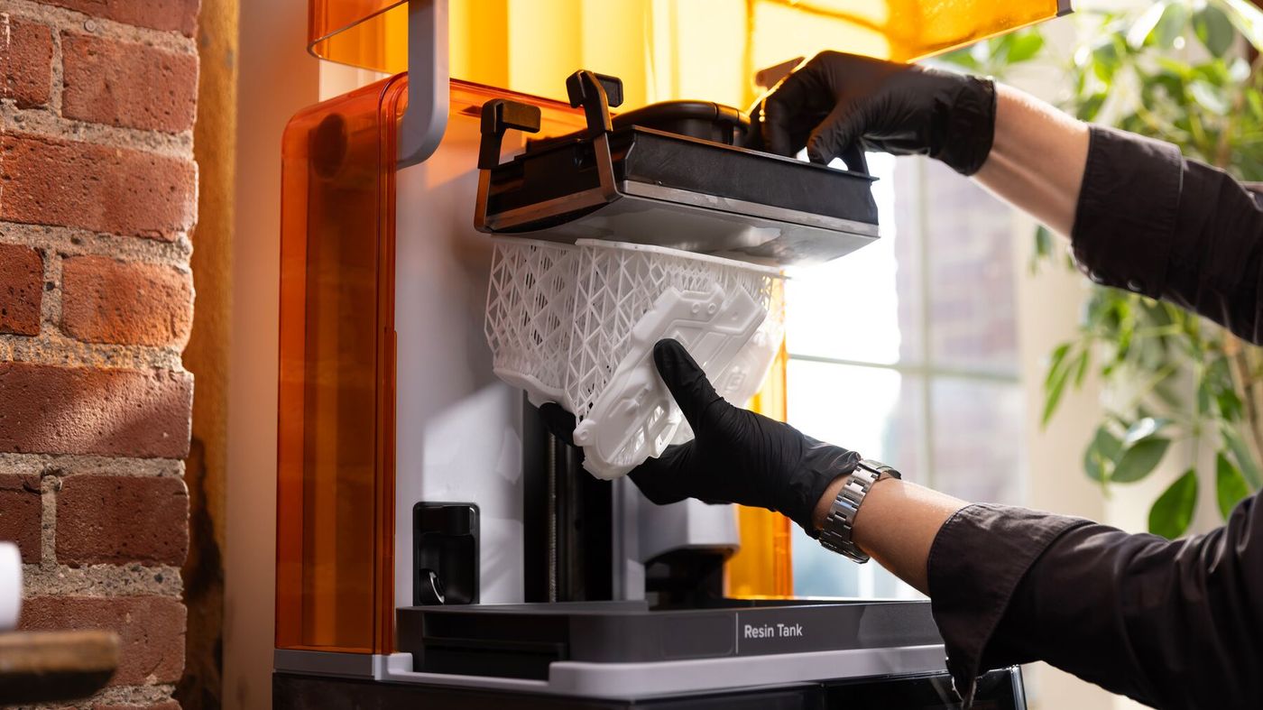 Gloved hands lowering a print on its build platform into the wash bucket