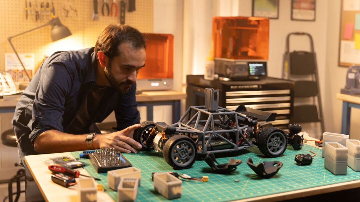 A builder assembling an RC car with printed parts in a home workshop