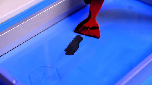 A red plastic scraper next to a flake of cured resin on a vat film