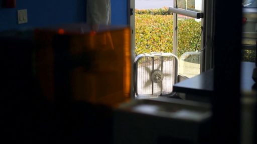 A box fan sits in an open doorway behind a resin printer