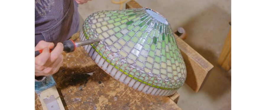 Person soldering a stained glass lampshade on a workbench