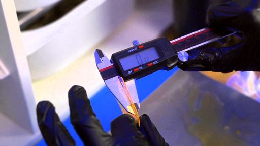 Gloved hands measure a thin resin test print with digital calipers
