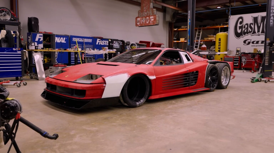 Red custom widebody sports car with unfinished body panels in a workshop