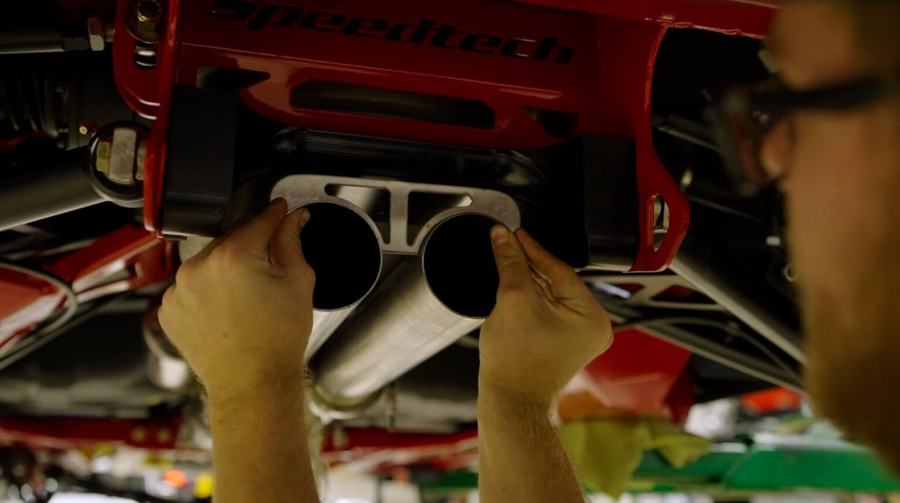 Person fitting dual exhaust tips under a red Speedtech car