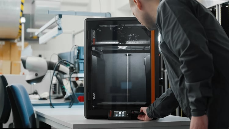A person is operating their Prusa CORE One L Critical Infrastructure 3D Printer in a factory facility.